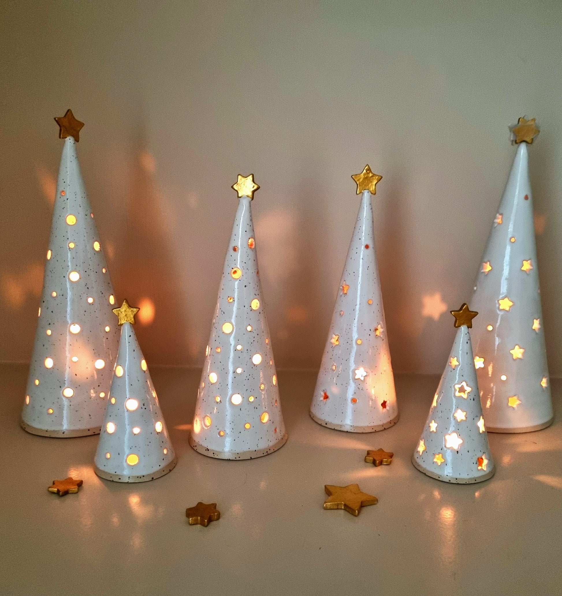 Group of handmade white ceramic Christmas trees. They have round or star cut outs for a magic glow.