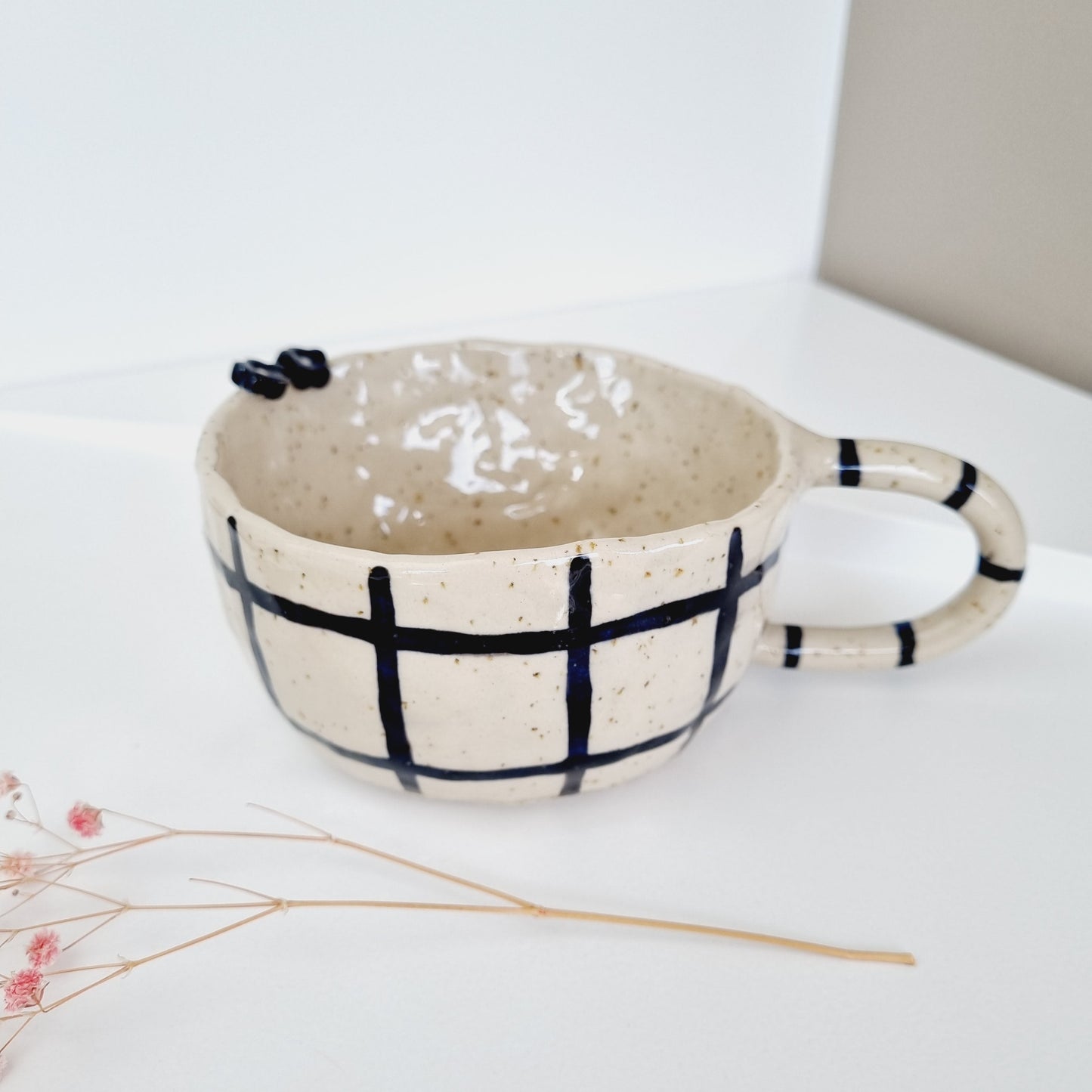 Handpainted gingham mug made from speckled clay. Decorated with a black gingham pattern. Three cute handpainted daisies inside
and two ceramic daisies on the rim