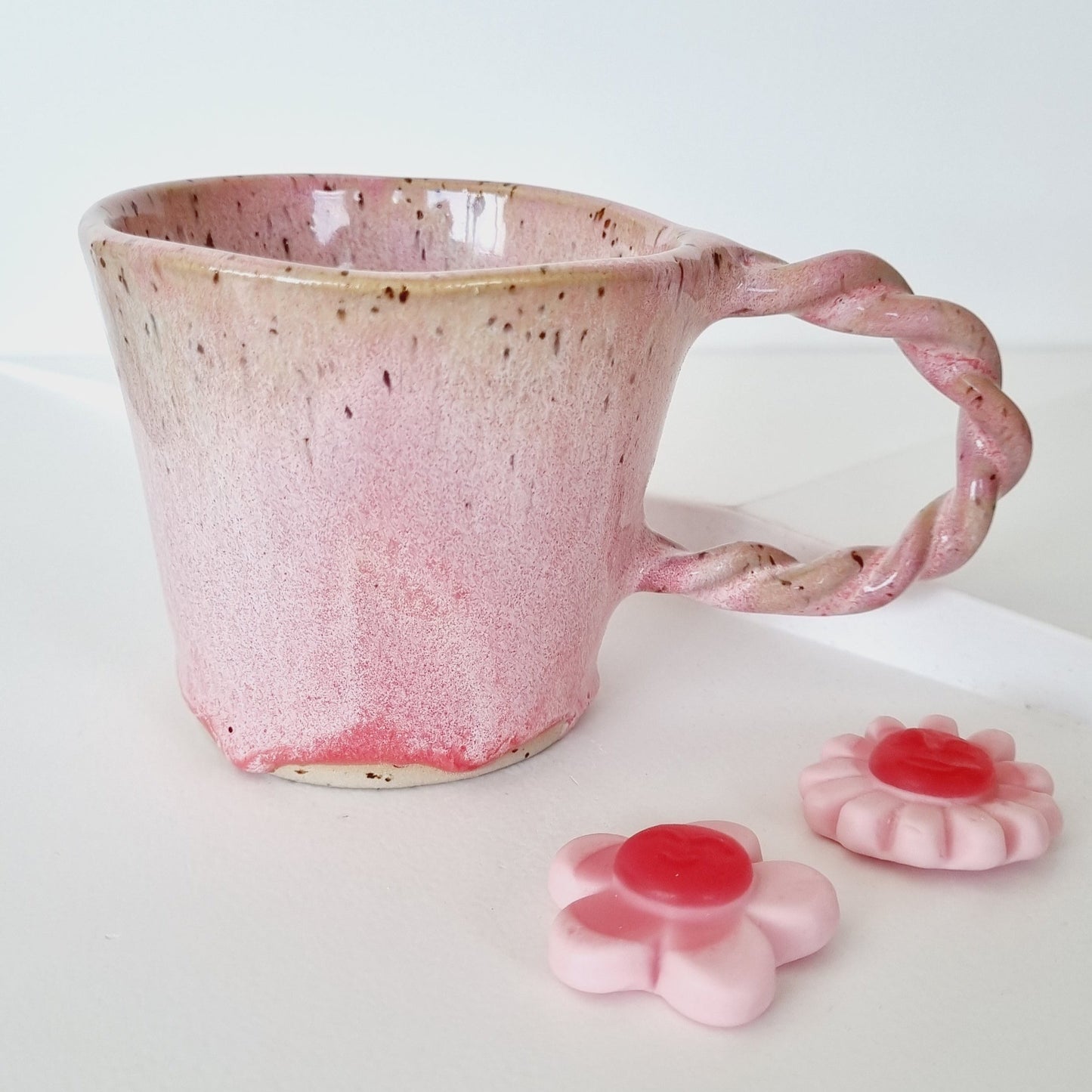 Handmade pink ceramic mug glazed with a pink drippy glaze. Braided handle