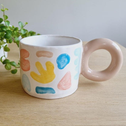 A colorful modern mug, handpainted with clorful geometric vectors. Bold donut handle.