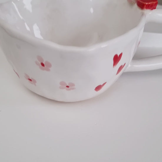 Heart shape mug, handpinched from a ball of clay. Painted with red hearts and pink daisies