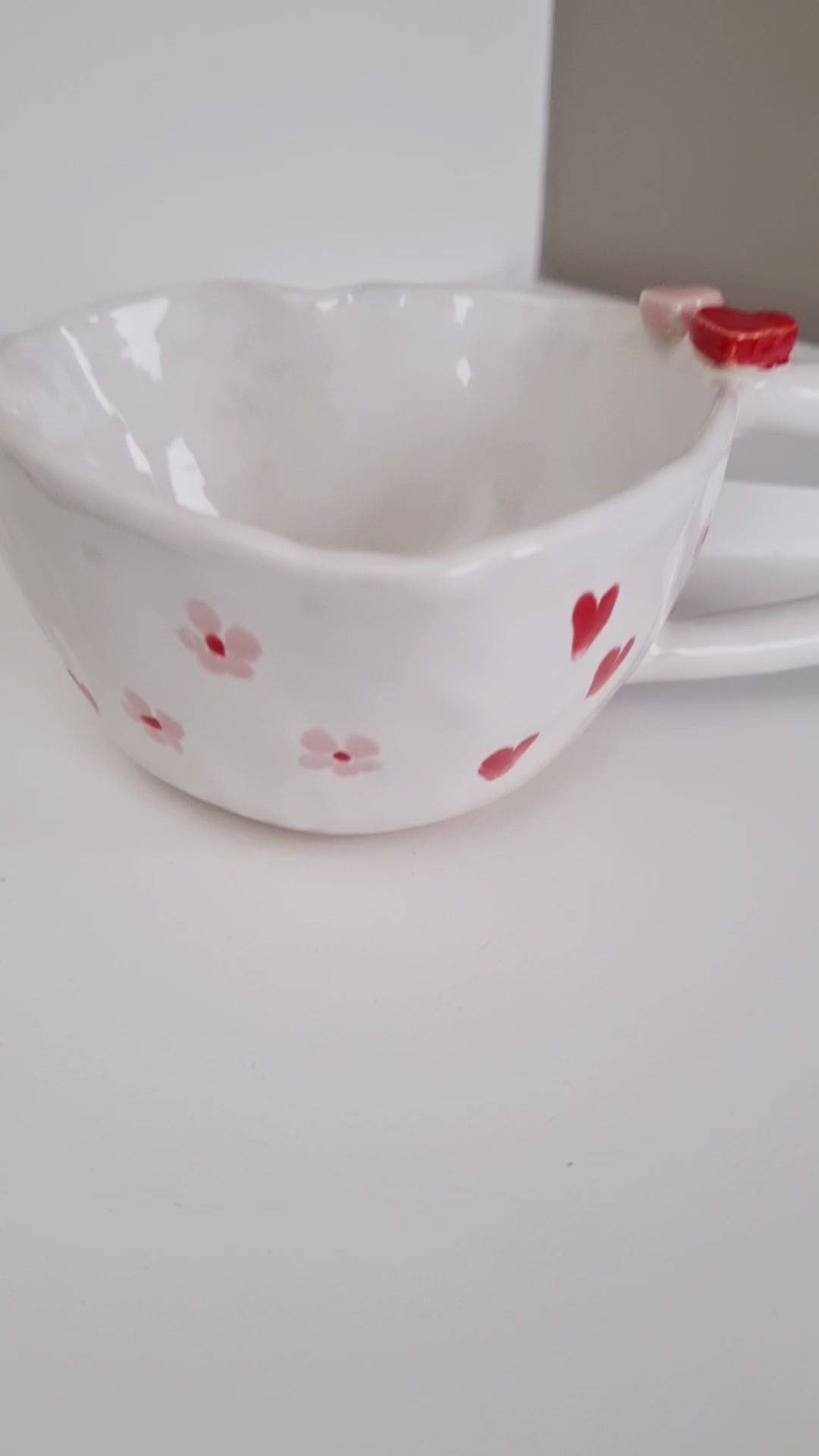 Heart shape mug, handpinched from a ball of clay. Painted with red hearts and pink daisies